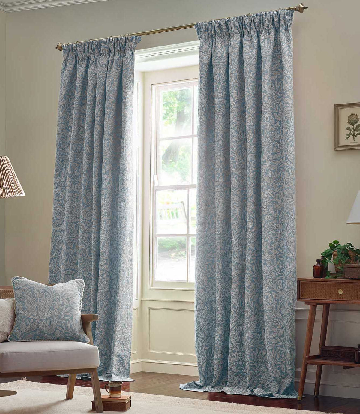 Morris & Co Acorn jacquard curtains in soft Wedgwood blue and off-white, framing a tall window in a bright living room with natural wood furniture.