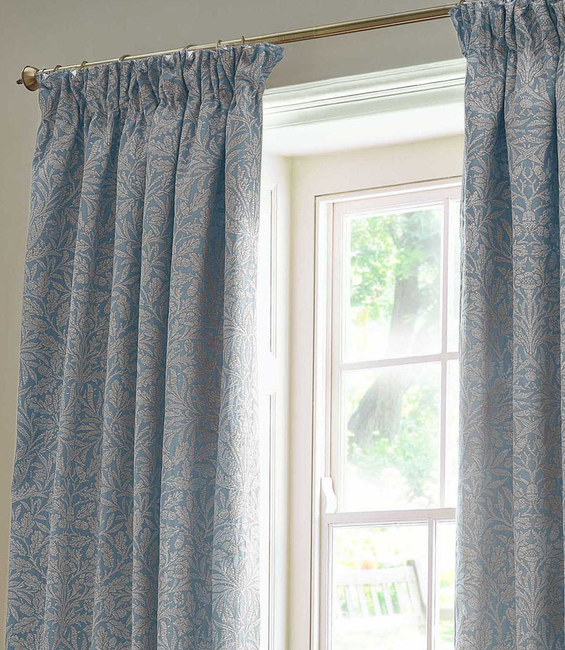 Close view of Morris & Co Acorn jacquard curtains in Wedgwood blue and off-white, showing the gathered pencil pleat heading and detailed acorn and foliage pattern.