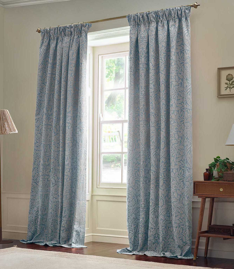 Pair of full-length Morris & Co Acorn jacquard curtains in Wedgwood blue and off-white, framing a tall window in a neutral living room.