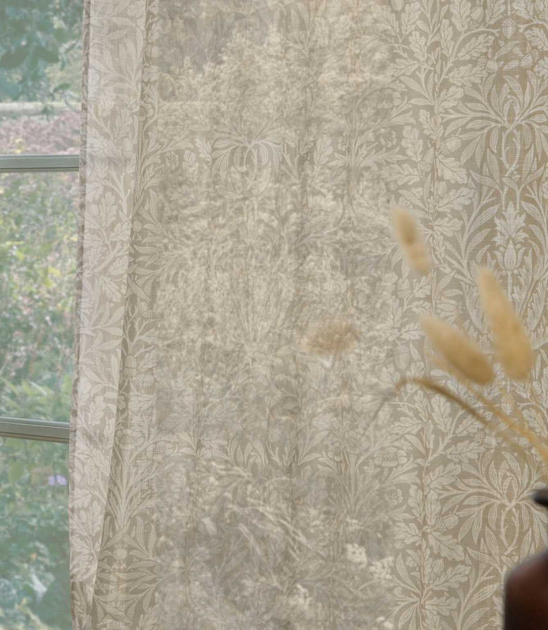 Close-up of Morris & Co Acorn sheer curtain fabric in soft cream and beige, showing the intricate acorn, leaf and floral pattern gently filtering natural light.