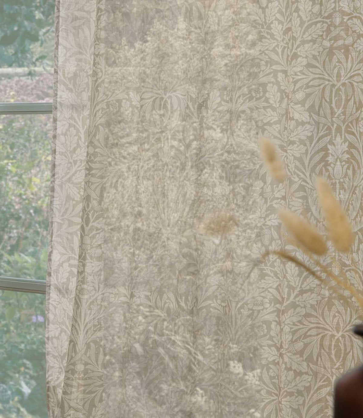 Close-up of Morris & Co Acorn sheer curtain fabric in soft cream and beige, showing the intricate acorn, leaf and floral pattern gently filtering natural light.