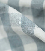 Detailed close-up of a fold in Aldsworth Check Haze fabric highlighting the textured weave and contrasting soft blue and white checked design.