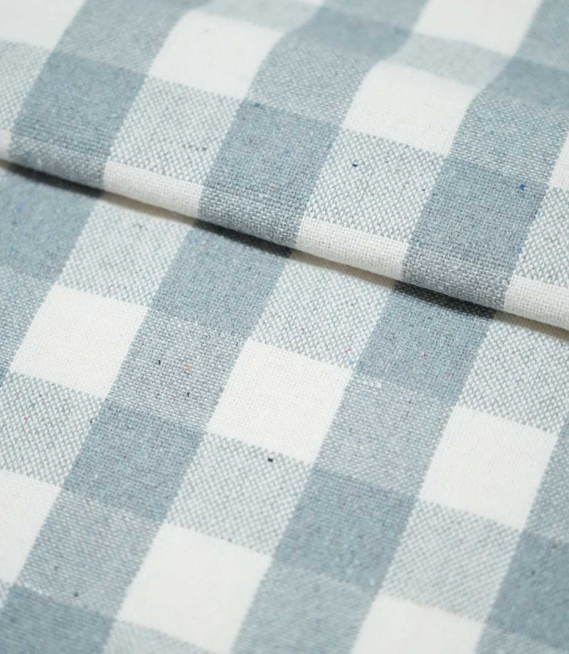 Folded Aldsworth Check Haze fabric displaying the repeating blue and white check pattern and textured woven surface across overlapping layers.