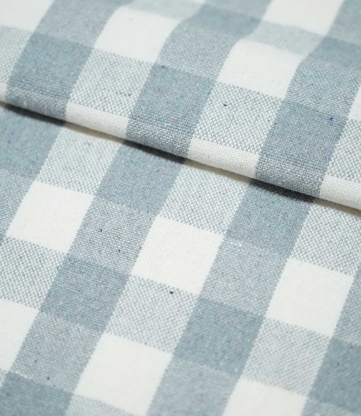 Folded Aldsworth Check Haze fabric displaying the repeating blue and white check pattern and textured woven surface across overlapping layers.
