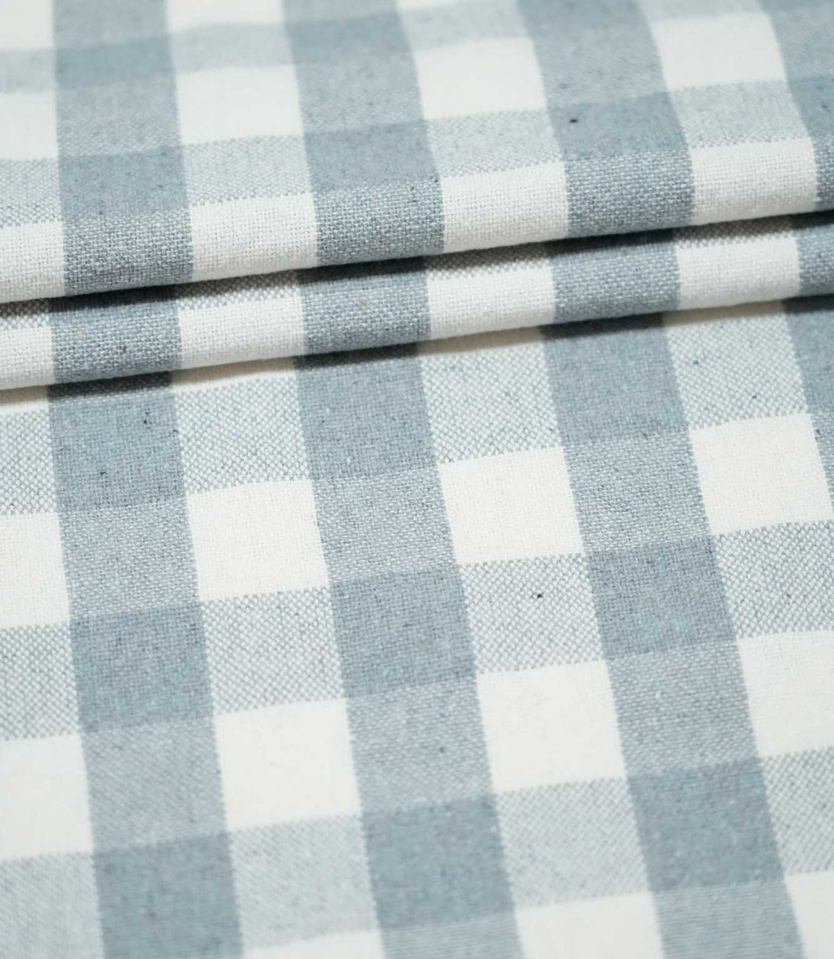 Layers of Aldsworth Check Haze fabric arranged in neat folds, showing the classic blue and white checks and subtle woven texture.