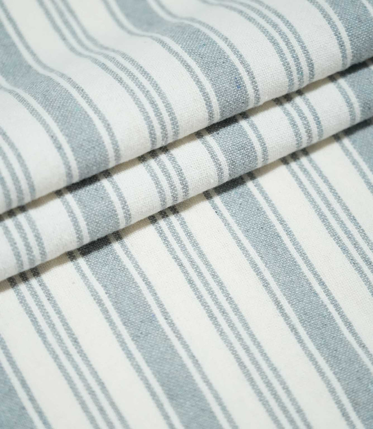 Folded Aldsworth Stripe Haze fabric featuring alternating wide and narrow blue-grey stripes on a white background with a textured weave.