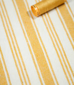Angled view of Aldsworth Stripe Ochre fabric with a coordinating golden yellow thread spool resting on the textured striped surface.