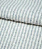 Folded Aldsworth Ticking Haze fabric showing classic blue-grey and white ticking stripes, with visible woven texture and subtle coloured flecks.
