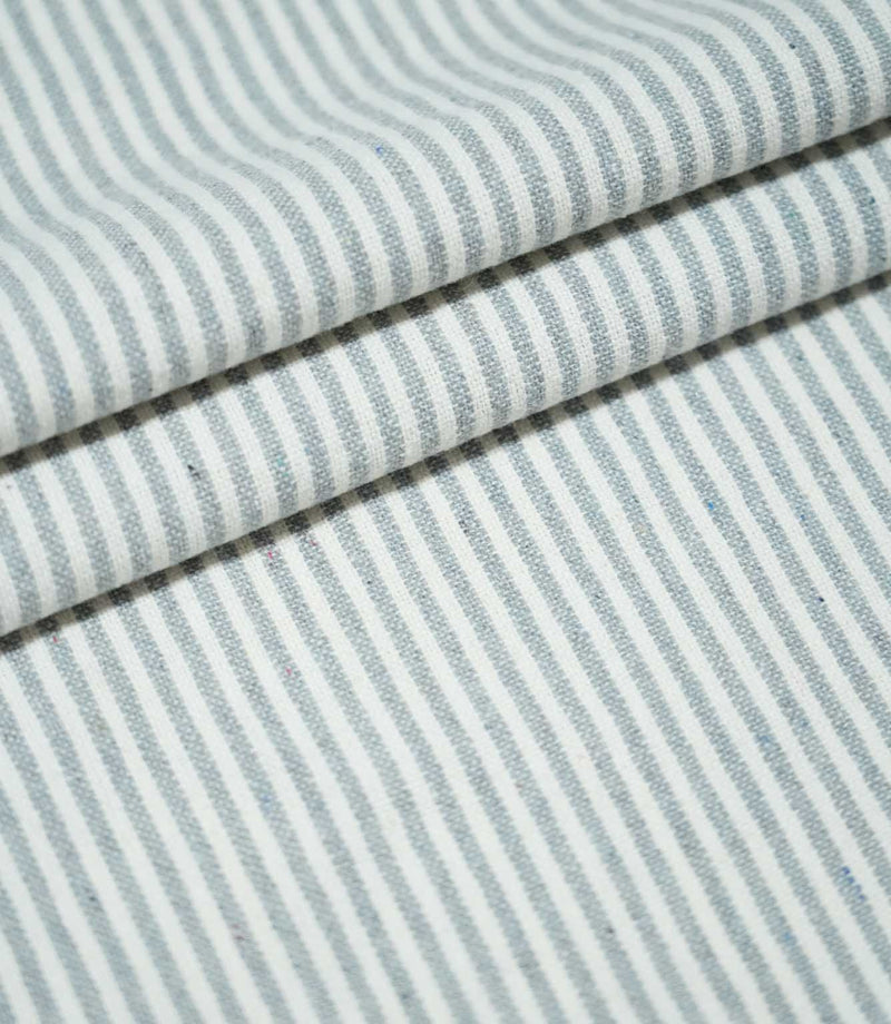 Aldsworth Ticking Haze fabric arranged in layered folds, showcasing its fine blue-grey and white striped pattern and textured woven surface.