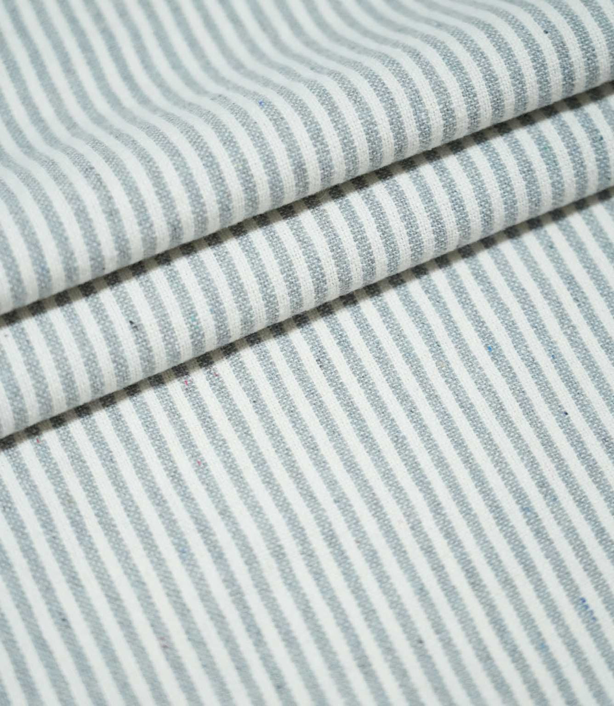 Aldsworth Ticking Haze fabric arranged in layered folds, showcasing its fine blue-grey and white striped pattern and textured woven surface.