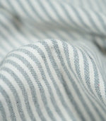Detailed close-up of Aldsworth Ticking Haze fabric gathered into a rounded fold, highlighting the blue-grey stripes, white detailing and textured weave.