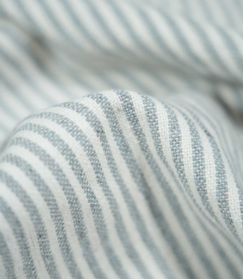 Detailed close-up of Aldsworth Ticking Haze fabric gathered into a rounded fold, highlighting the blue-grey stripes, white detailing and textured weave.