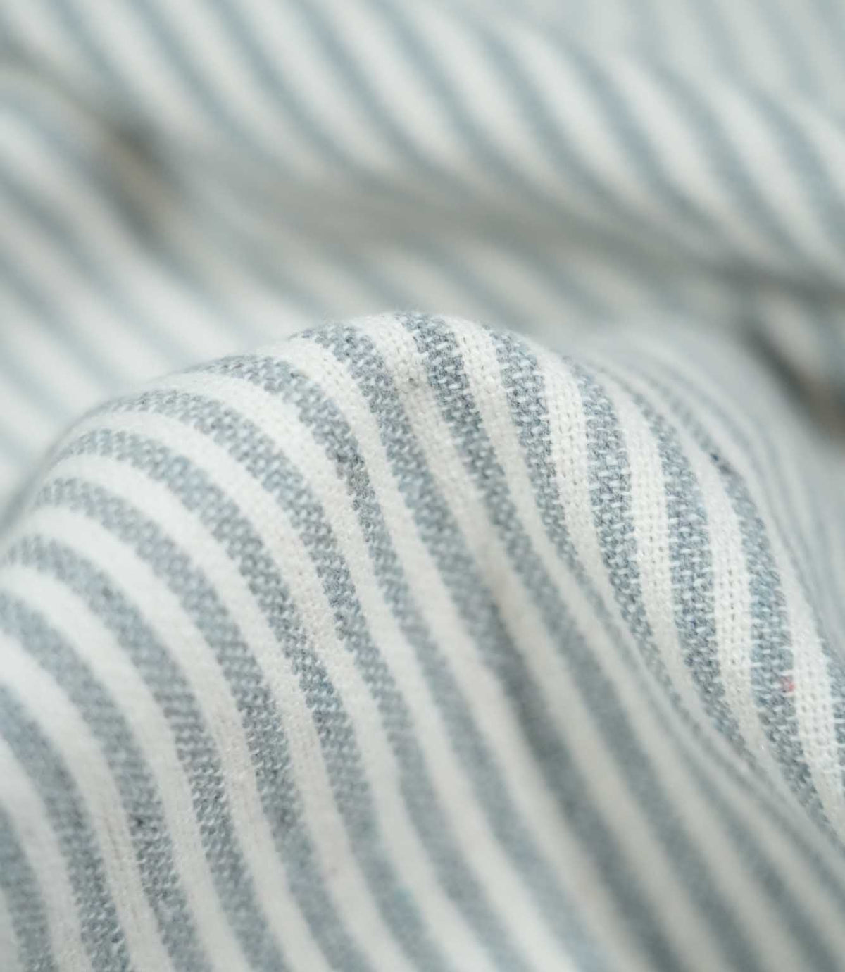Detailed close-up of Aldsworth Ticking Haze fabric gathered into a rounded fold, highlighting the blue-grey stripes, white detailing and textured weave.