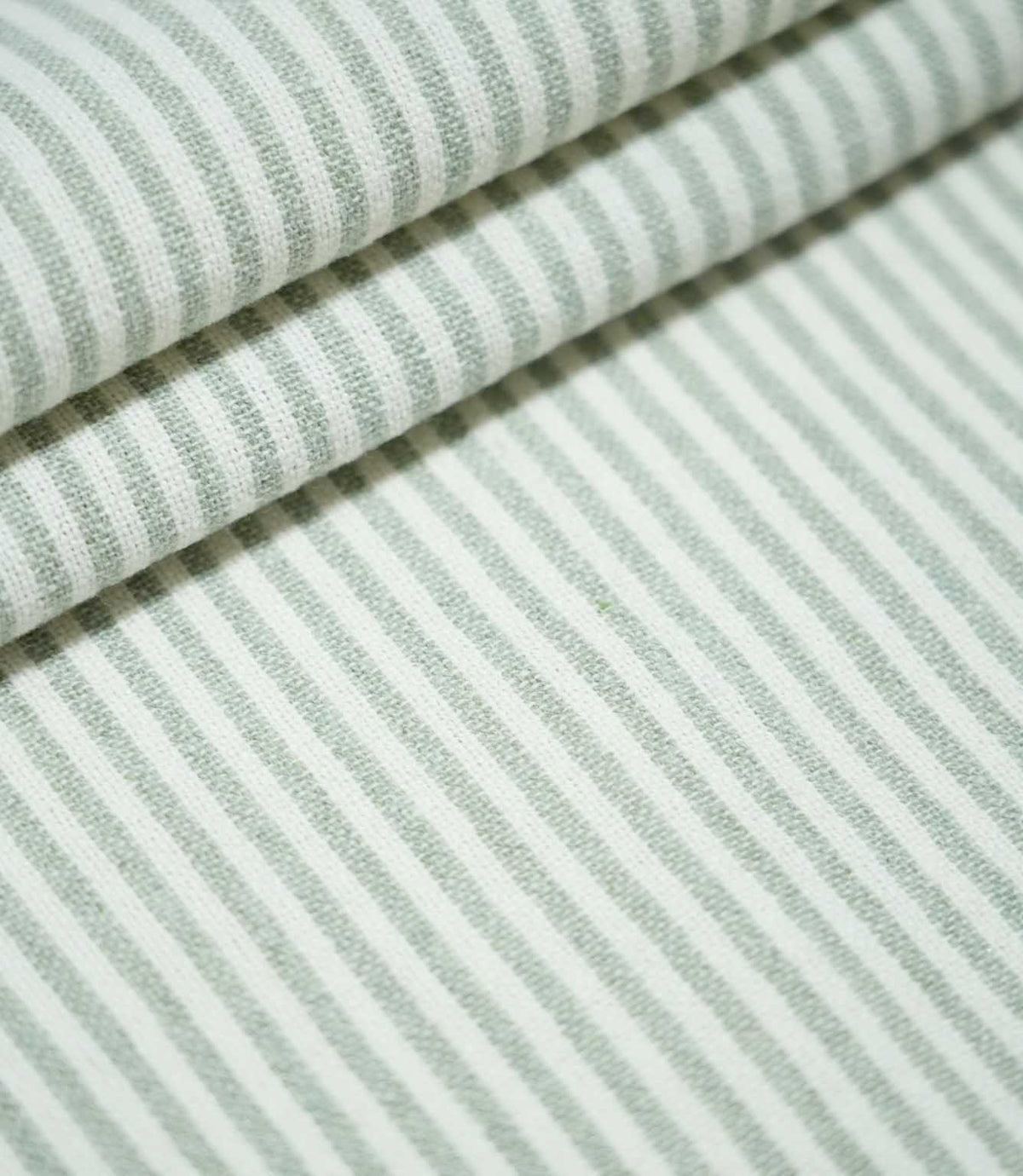 Aldsworth Ticking Mint fabric arranged in layered folds, showcasing its narrow green and white striped pattern and textured woven surface.