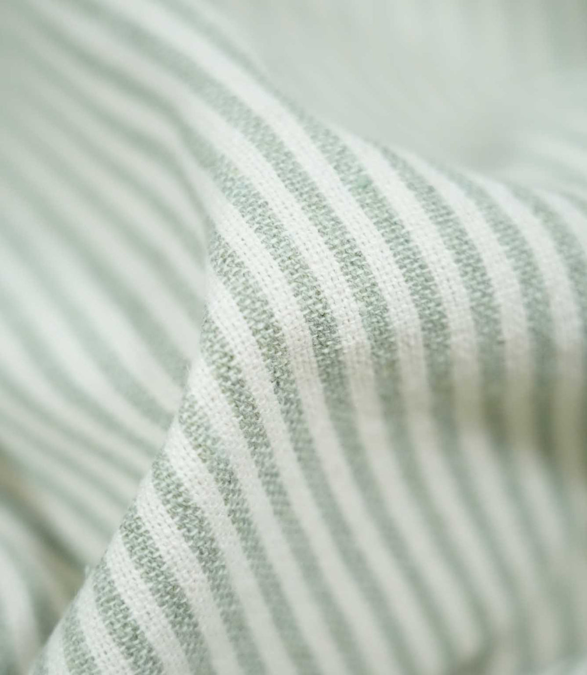 Detailed close-up of Aldsworth Ticking Mint fabric gathered into a raised fold, highlighting its pale green stripes, white detailing and textured weave.