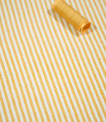 Aldsworth Ticking Ochre striped fabric with a coordinating golden yellow thread spool, highlighting the fine vertical stripes and woven texture.
