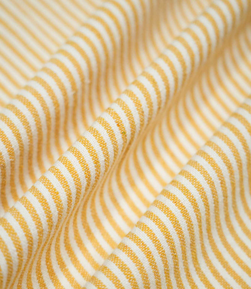 Aldsworth Ticking Ochre fabric arranged in soft, flowing folds, showing the narrow golden yellow ticking stripes and natural drape.