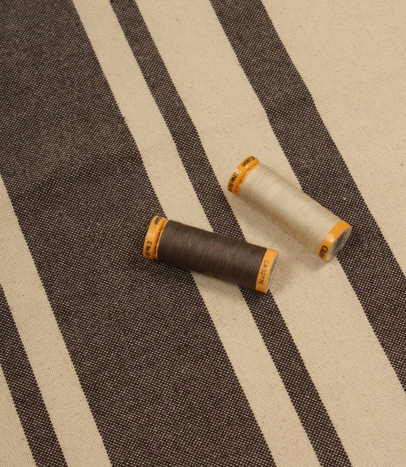 Brown striped furnishing fabric with natural tones, shown with coordinating thread reels to highlight colour matching.