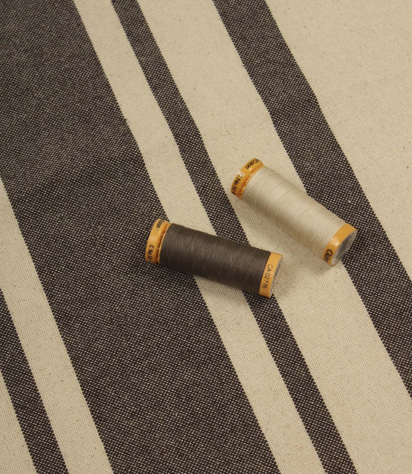 Brown striped furnishing fabric with natural tones, shown with coordinating thread reels to highlight colour matching.
