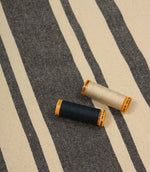 Charcoal striped furnishing fabric displayed with coordinating thread reels to highlight colour matching and texture.