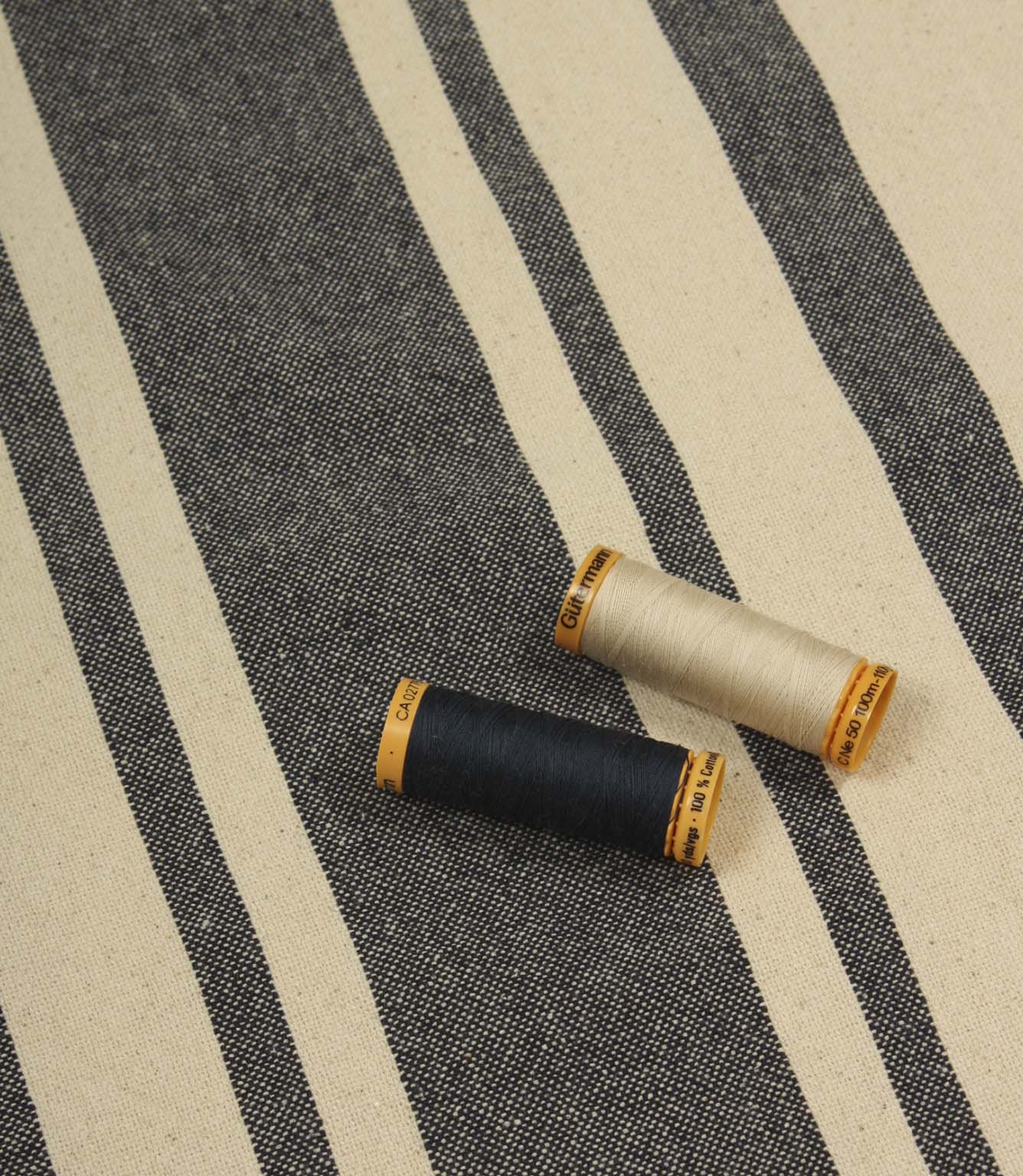 Charcoal striped furnishing fabric displayed with coordinating thread reels to highlight colour matching and texture.