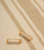 Beige striped upholstery fabric with matching thread reels displayed on the fabric surface.