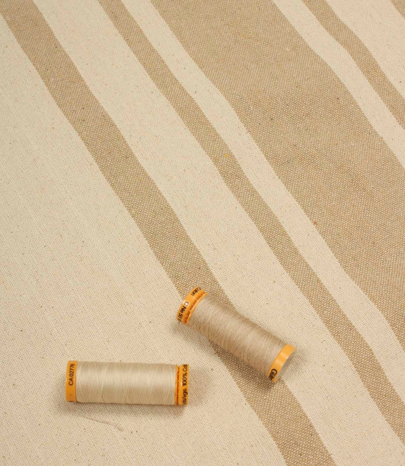 Beige striped upholstery fabric with matching thread reels displayed on the fabric surface.