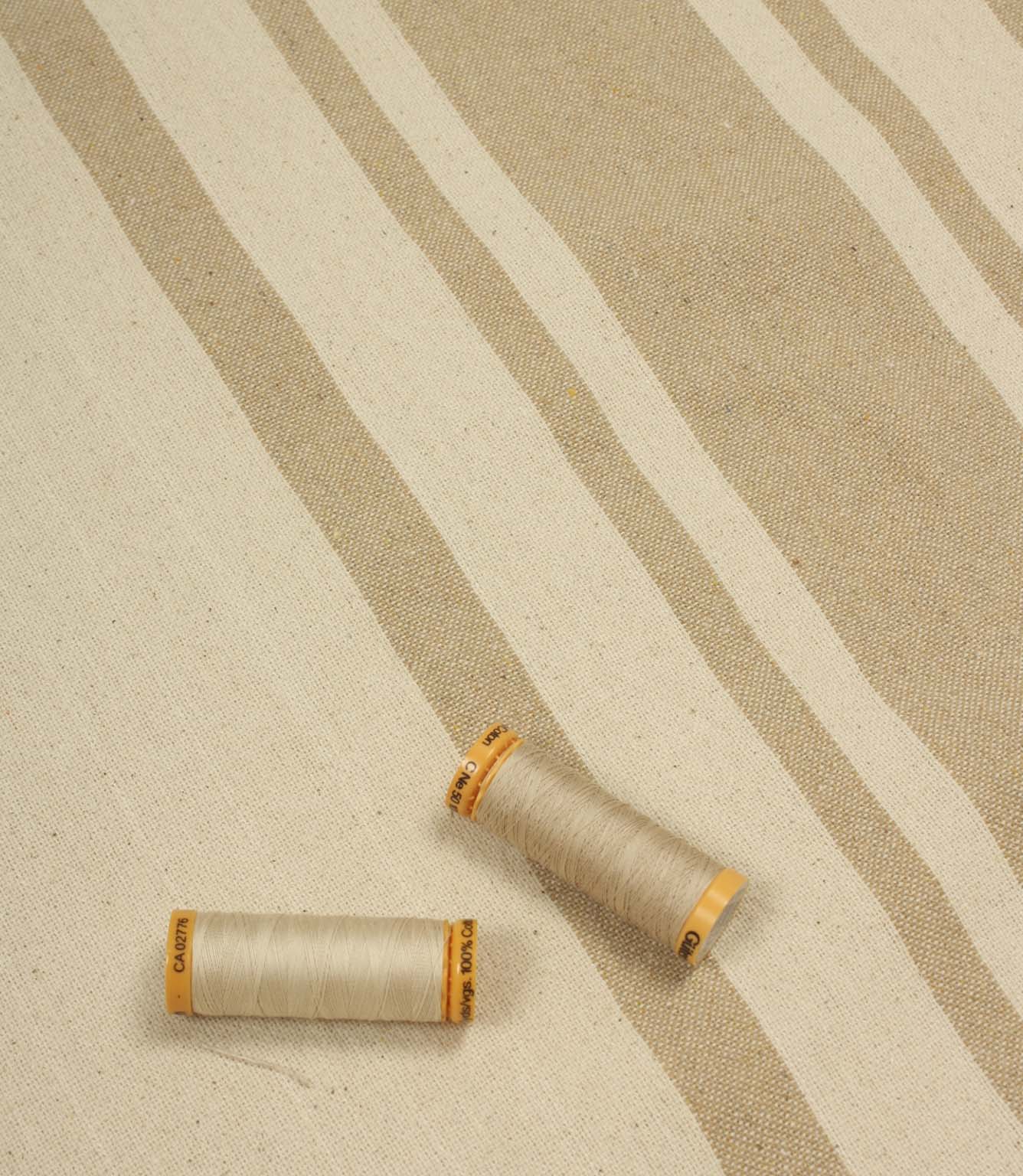 Beige striped upholstery fabric with matching thread reels displayed on the fabric surface.