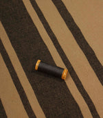 Black striped furnishing fabric displayed with coordinating thread reel to show colour matching and woven texture.