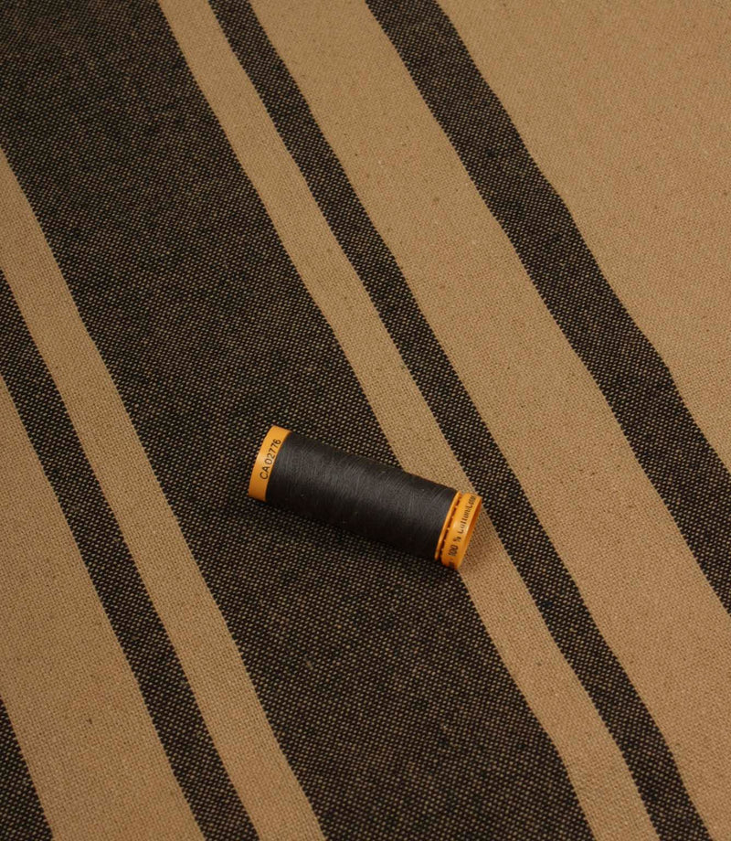 Black striped furnishing fabric displayed with coordinating thread reel to show colour matching and woven texture.