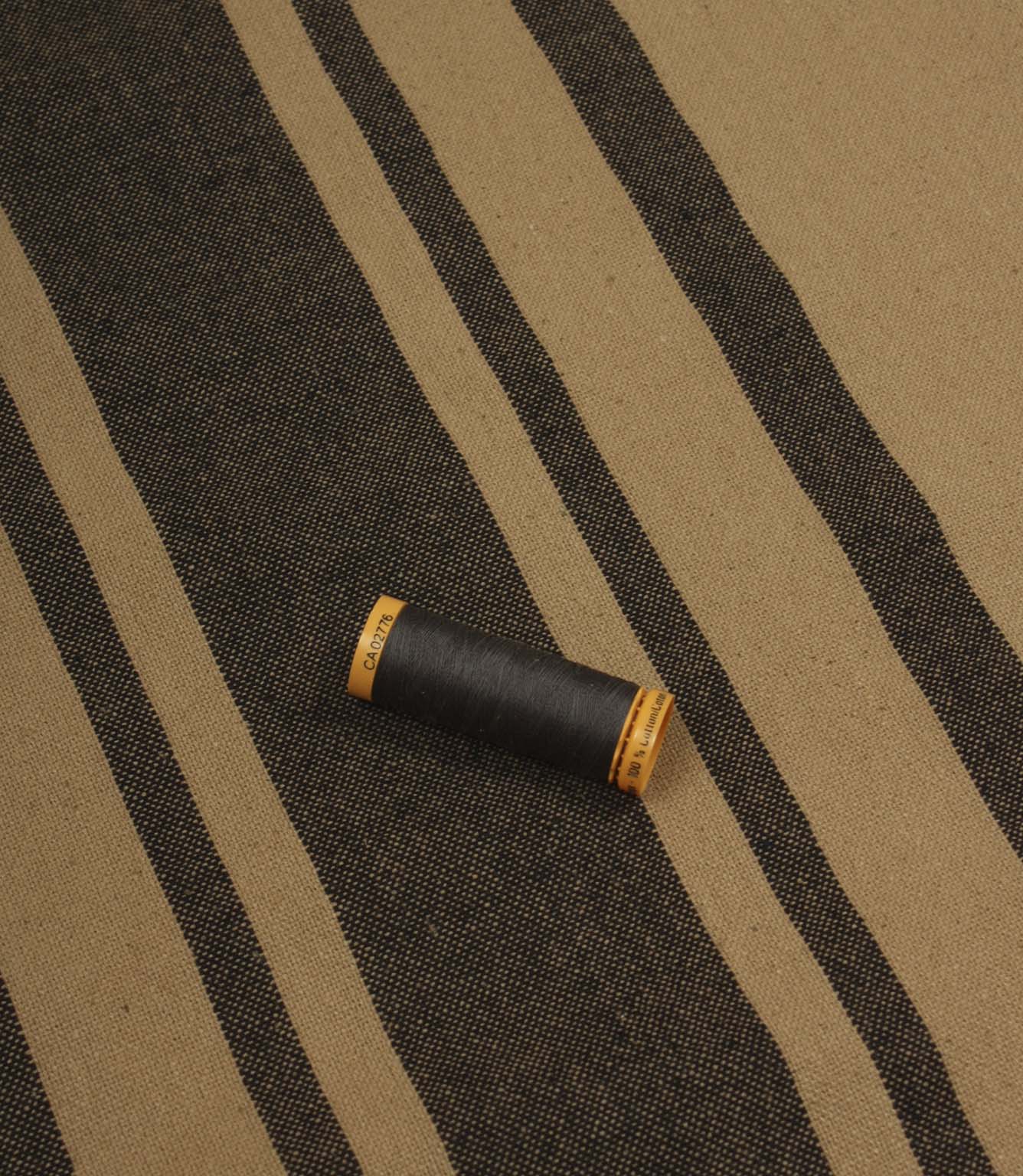 Black striped furnishing fabric displayed with coordinating thread reel to show colour matching and woven texture.