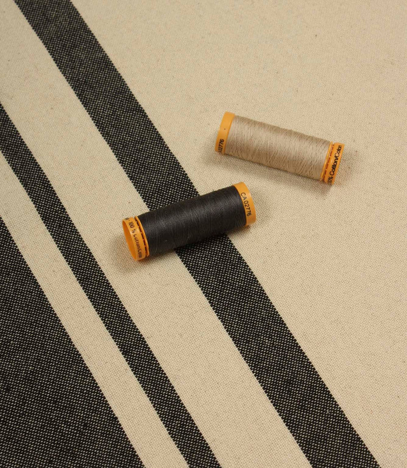 Cream and black stripe furnishing fabric displayed with matching thread reels to highlight colour coordination and weave detail.