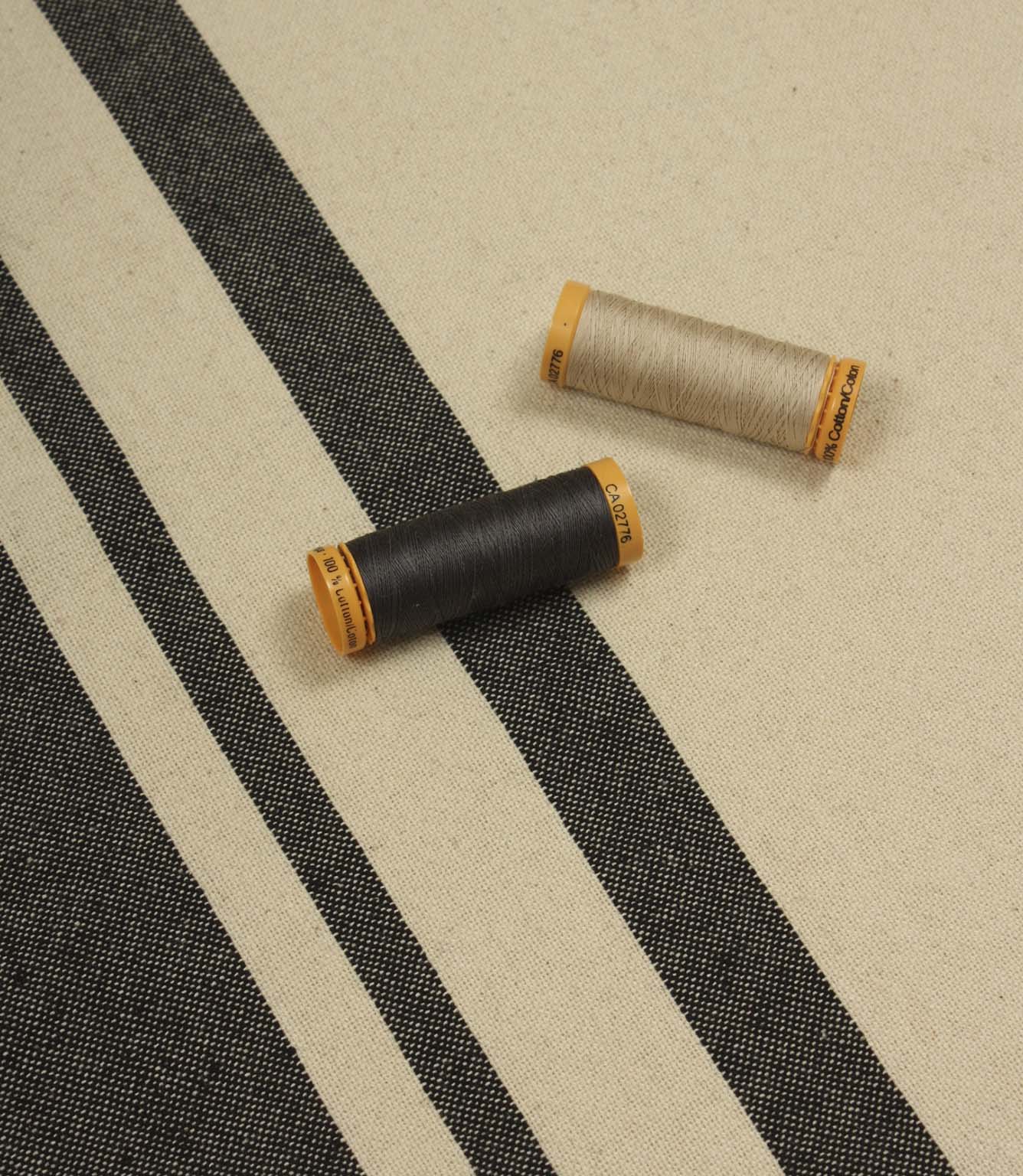 Cream and black stripe furnishing fabric displayed with matching thread reels to highlight colour coordination and weave detail.
