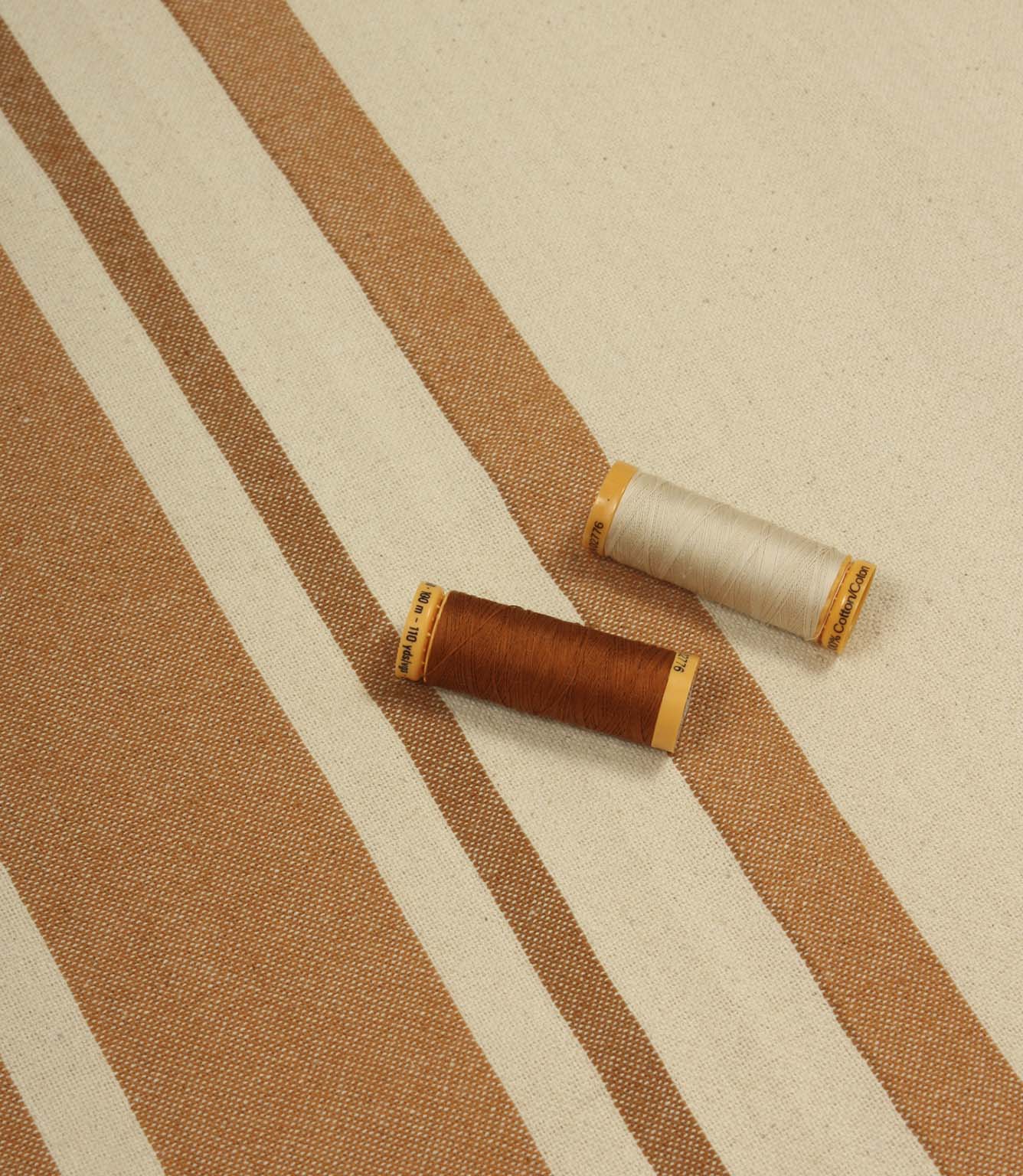 Cream and terracotta striped furnishing fabric displayed with matching thread reels to showcase colour and weave detail.