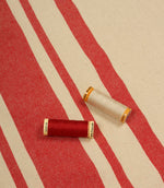 Cream and red striped furnishing fabric displayed with matching thread reels to showcase colour coordination and weave detail.