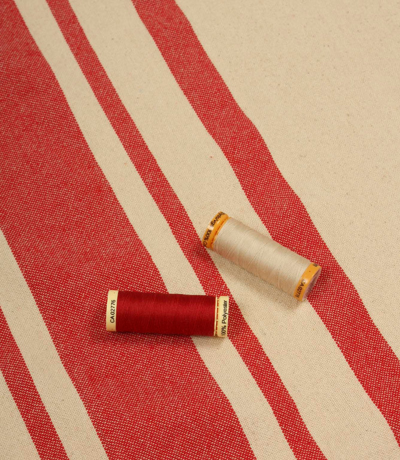 Cream and red striped furnishing fabric displayed with matching thread reels to showcase colour coordination and weave detail.