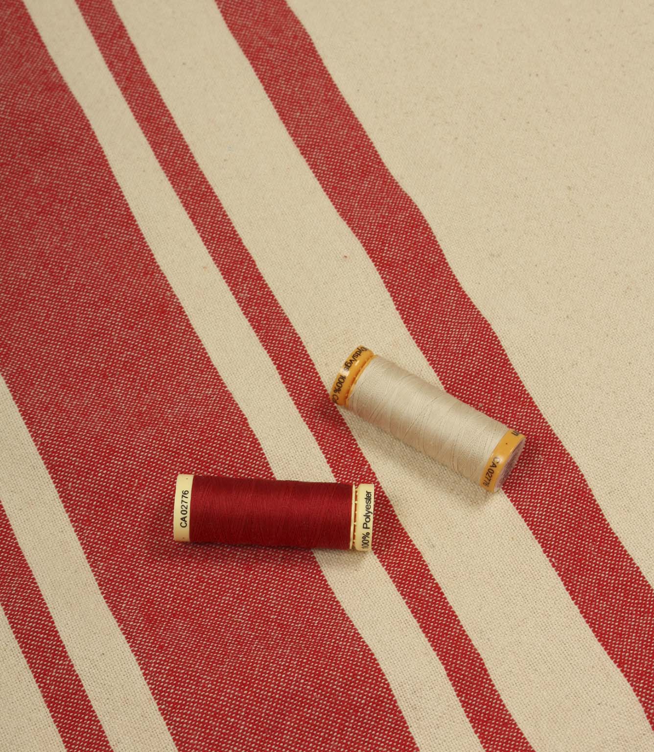 Cream and red striped furnishing fabric displayed with matching thread reels to showcase colour coordination and weave detail.