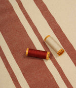 Cream and terracotta striped furnishing fabric displayed with matching thread reels to highlight colour coordination and fabric texture.