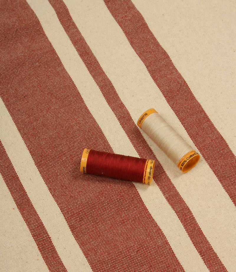 Cream and terracotta striped furnishing fabric displayed with matching thread reels to highlight colour coordination and fabric texture.