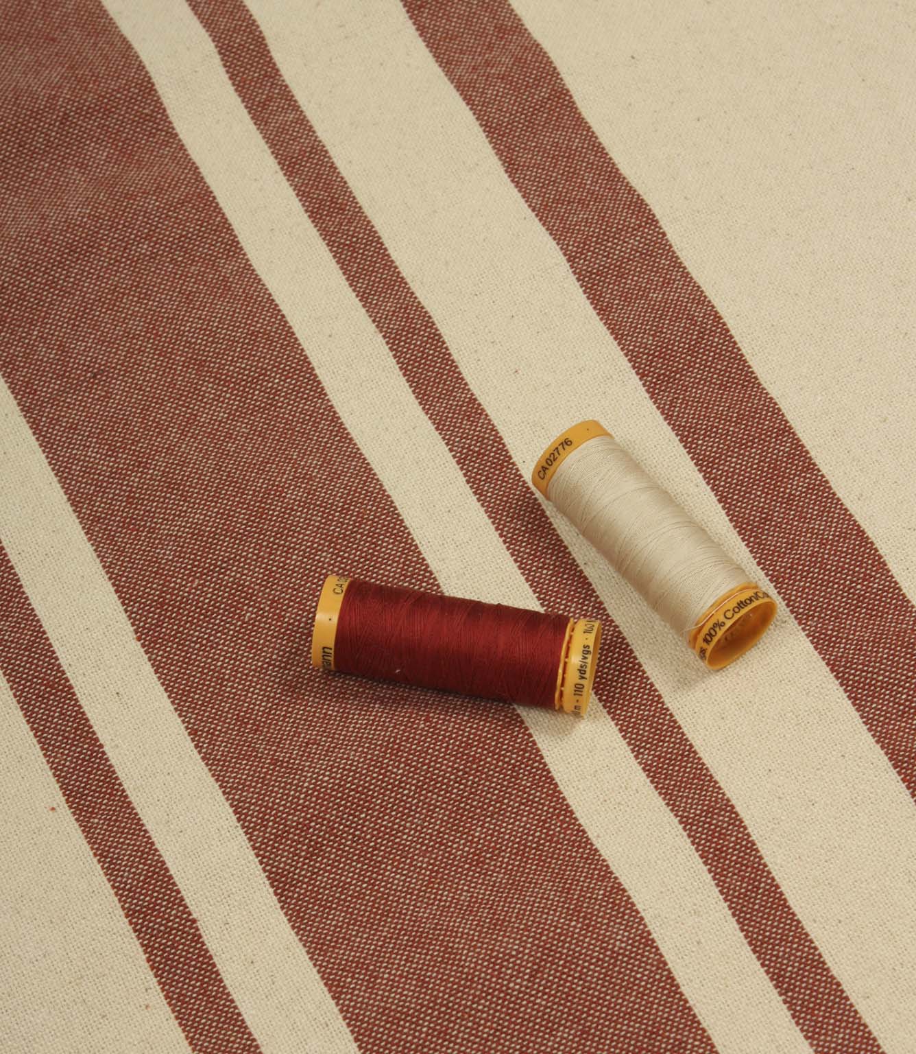 Cream and terracotta striped furnishing fabric displayed with matching thread reels to highlight colour coordination and fabric texture.
