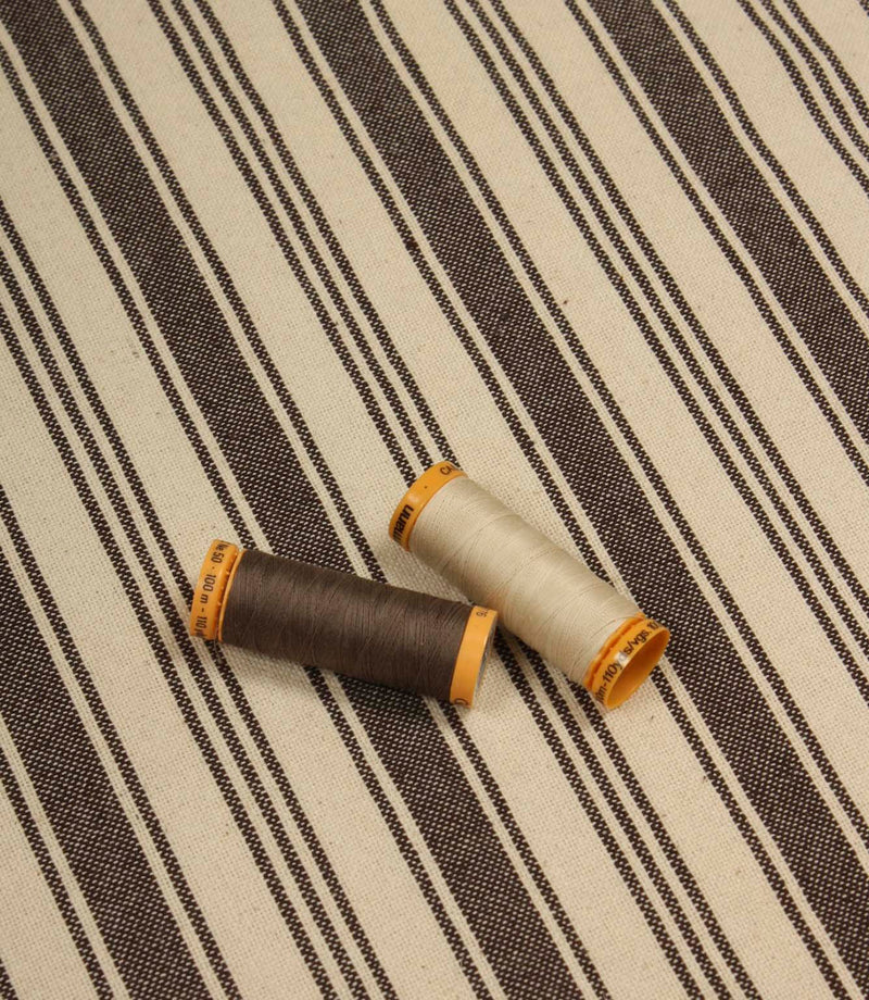 Cream and dark brown striped furnishing fabric displayed with coordinating thread reels to highlight colour matching and weave detail.