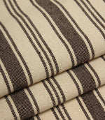 Detailed close-up of folded cream and dark brown striped fabric with contrasting stripe widths and textured weave.