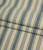 Folded blue and cream striped fabric showcasing the soft drape and woven texture of the classic ticking stripe pattern.