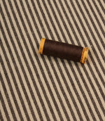 Brown striped upholstery fabric displayed with matching thread spool for colour coordination.