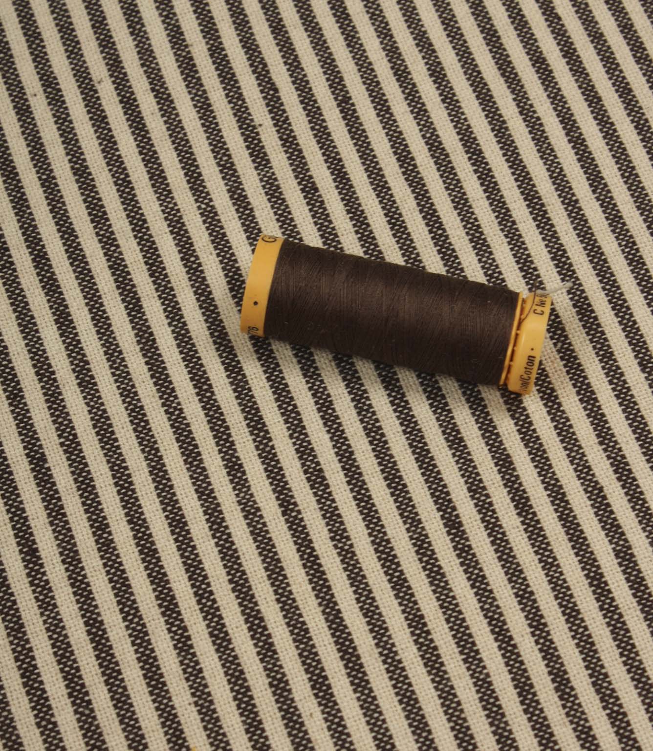 Brown striped upholstery fabric displayed with matching thread spool for colour coordination.