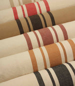 Collection of striped upholstery and curtain fabrics arranged in horizontal rolls, showcasing classic woven stripe designs in soft neutral and earthy tones.