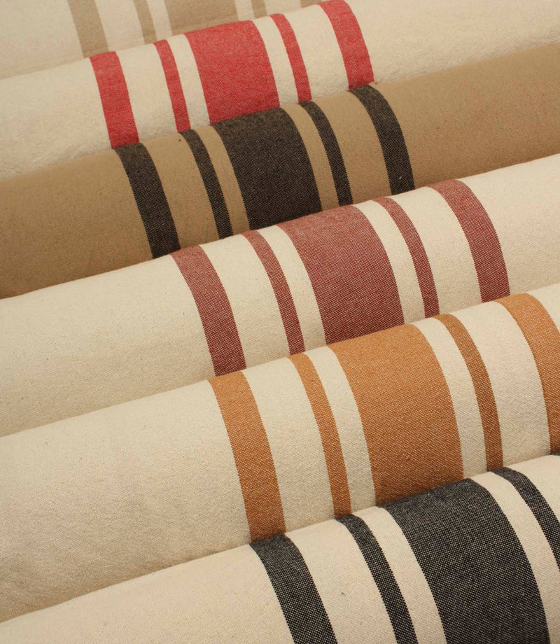 Collection of striped upholstery and curtain fabrics arranged in horizontal rolls, showcasing classic woven stripe designs in soft neutral and earthy tones.
