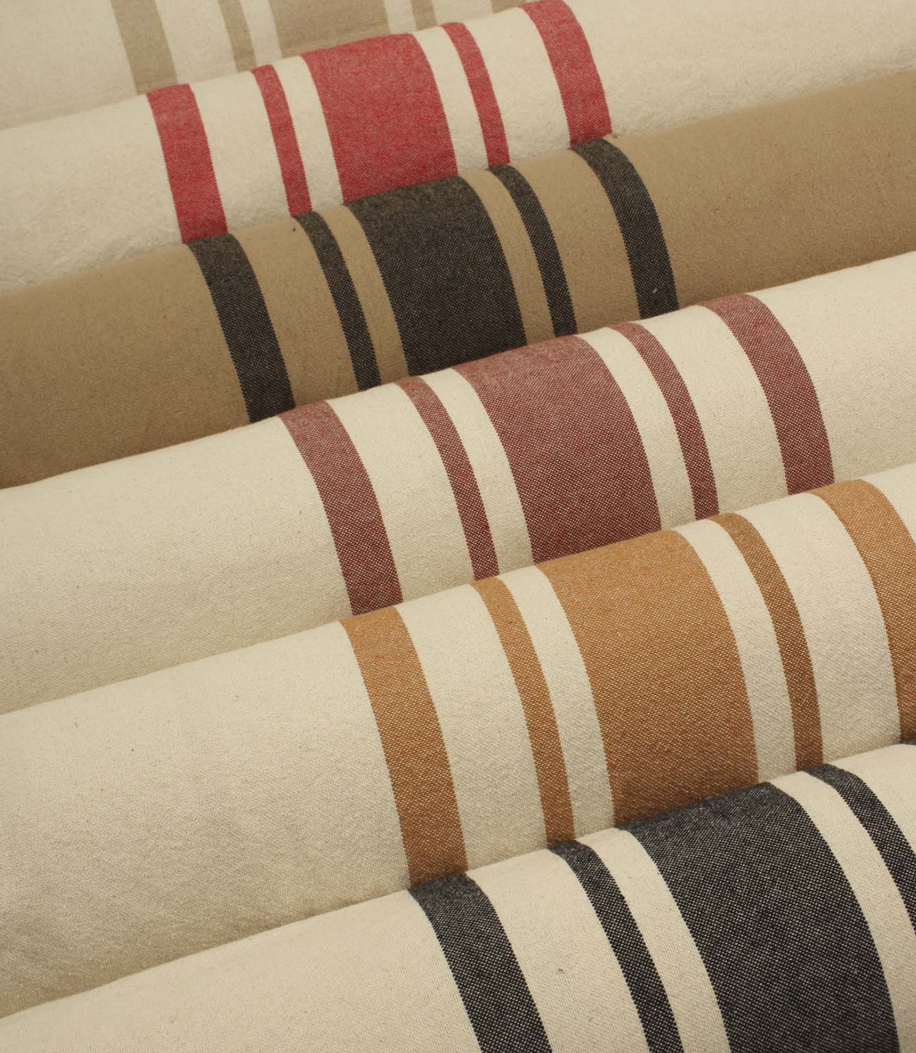 Collection of striped upholstery and curtain fabrics arranged in horizontal rolls, showcasing classic woven stripe designs in soft neutral and earthy tones.