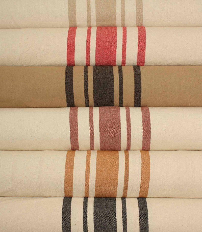 Close-up of rolled striped fabrics highlighting the textured weave and bold stripe patterns in ochre, rose pink, and charcoal against natural cream backgrounds.