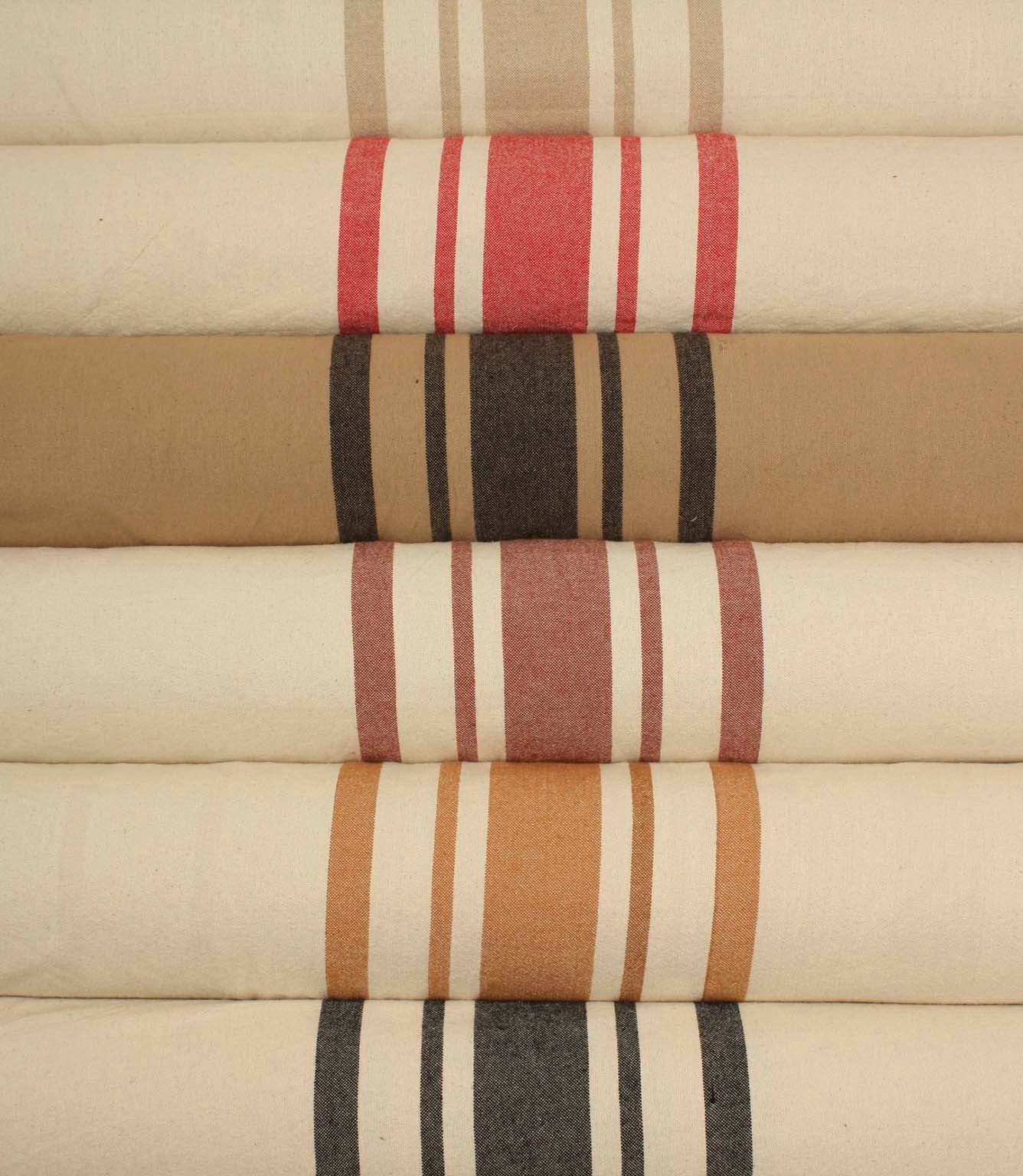 Close-up of rolled striped fabrics highlighting the textured weave and bold stripe patterns in ochre, rose pink, and charcoal against natural cream backgrounds.